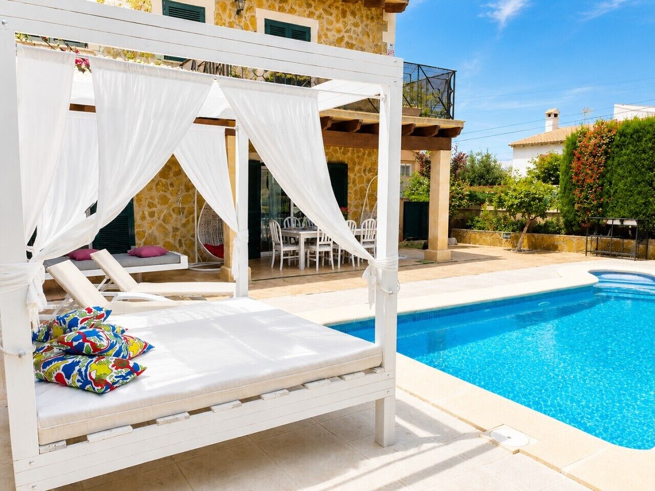 A white canopy bed with colorful pillows, a pool, and a patio area with outdoor furniture.