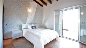 Une chambre à coucher comprenant un lit, une table de chevet, une commode, une fenêtre et une porte.