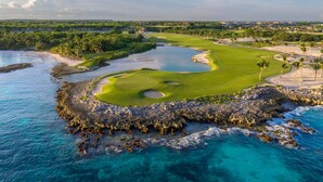 A coastal golf course with a water hazard, sand bunkers, and a clear view of the ocean. - Cozy 1BR w Balcony Pool Beach Access Cap Cana (Punta Cana)