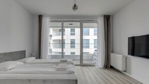 A modern hotel room with a large bed, a TV, and a balcony with a view of the building. - Studio Sw. Piotra by Grand Apartments (Gdynia)