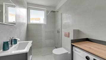 A modern bathroom with a shower, toilet, sink, and a built-in washing machine.