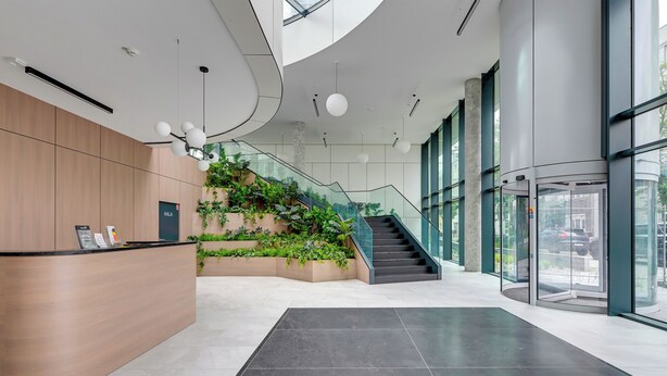 A modern reception area with a wooden desk, a staircase with greenery, and a glass elevator. - Studio Sw. Piotra by Grand Apartments (Gdynia)