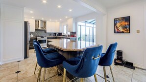 Une cuisine moderne avec un îlot central, deux chaises en velours bleu et une grande fenêtre.