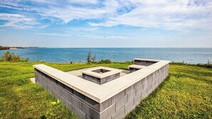 Une structure en béton avec une surface plane et une découpe rectangulaire, entourée d’herbe et donnant sur une étendue d’eau.