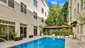 A swimming pool surrounded by a building with multiple windows and potted plants. - Pool & Jacuzzi! Walk to beach, South Point Pier, (Miami Beach)