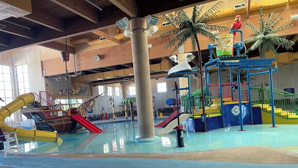 Ein Indoor-Wasserpark mit Rutschen, einem Spielbereich im Schiffsdesign und einer Palmen-Dekoration.