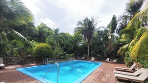 En træterrasse med swimmingpool, omgivet af frodig vegetation og palmer.