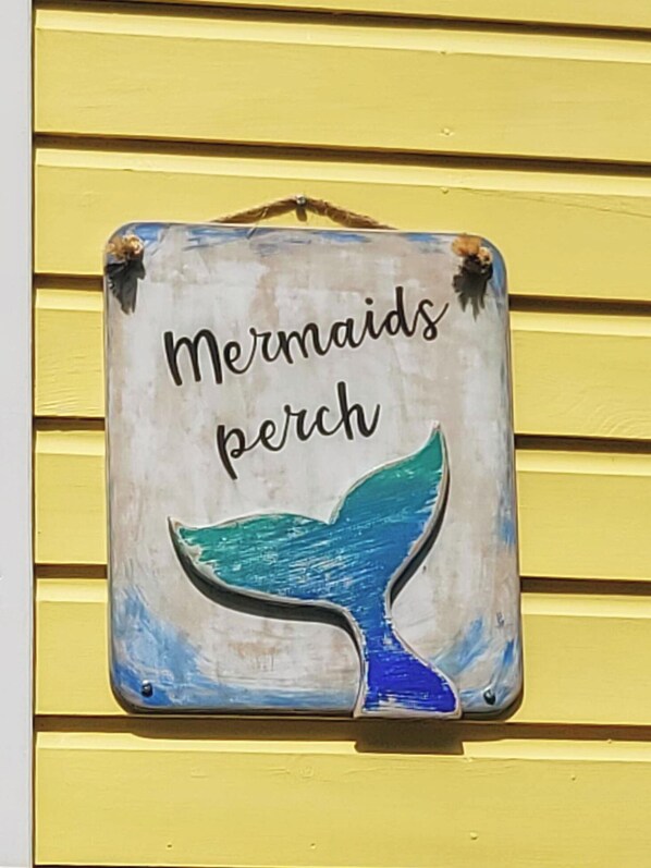 Un letrero con el texto 'Mermaids perch' e una cola de sirena pintada.