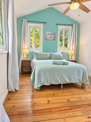 A bedroom with a bed, two bedside tables, a ceiling fan, and two windows with curtains. - Cozy Cabana, 1-Minute Walk to the beach and Pool & Budget-Friendly! (Roatan)