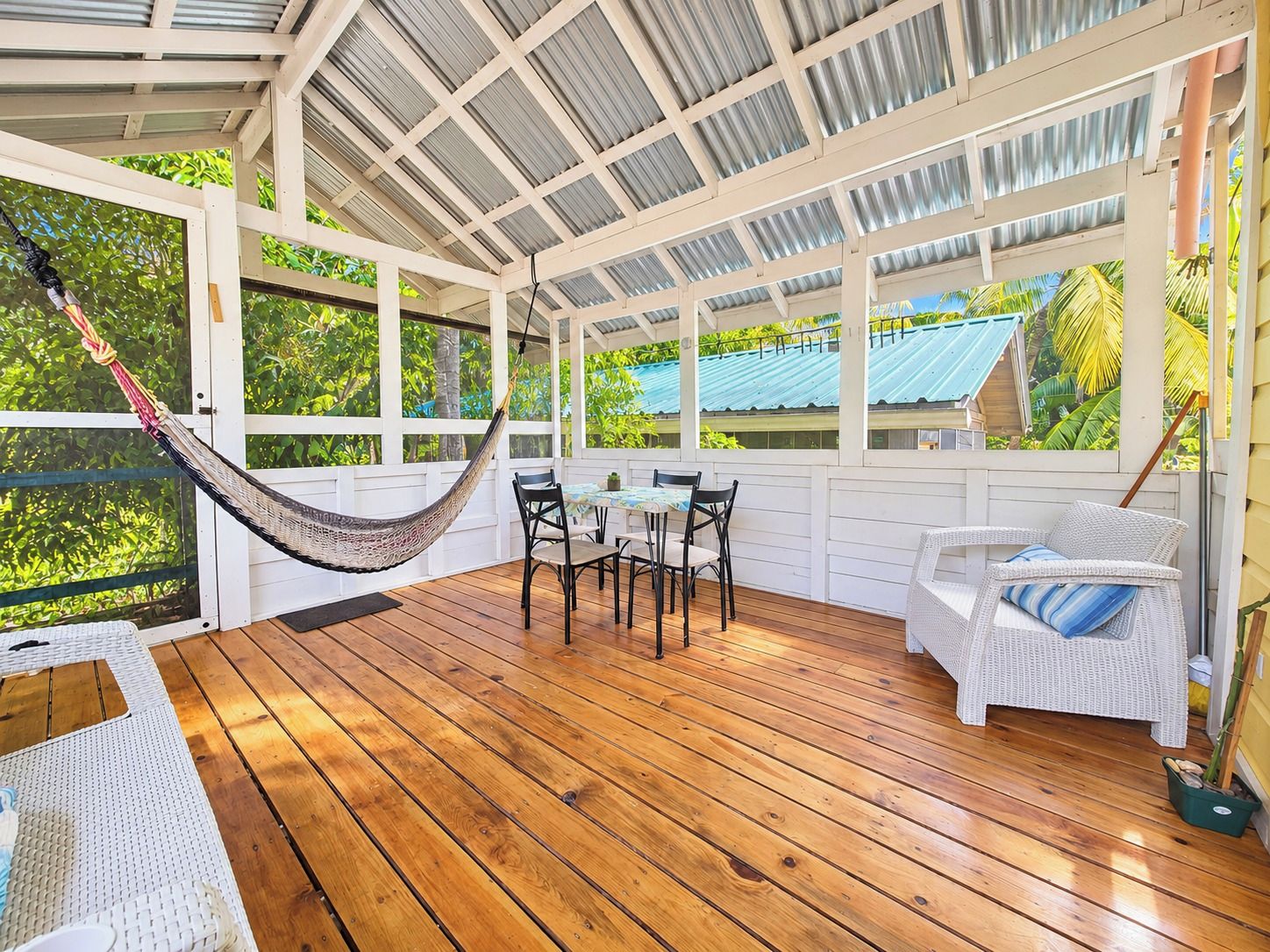 A covered outdoor area with a wooden floor, a hammock, a table with chairs, and a white sofa.