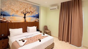 A modern bedroom with a large bed, a painting of a tree, an air conditioning unit, and a brown curtain. - Olivia Hotel (Cairo)