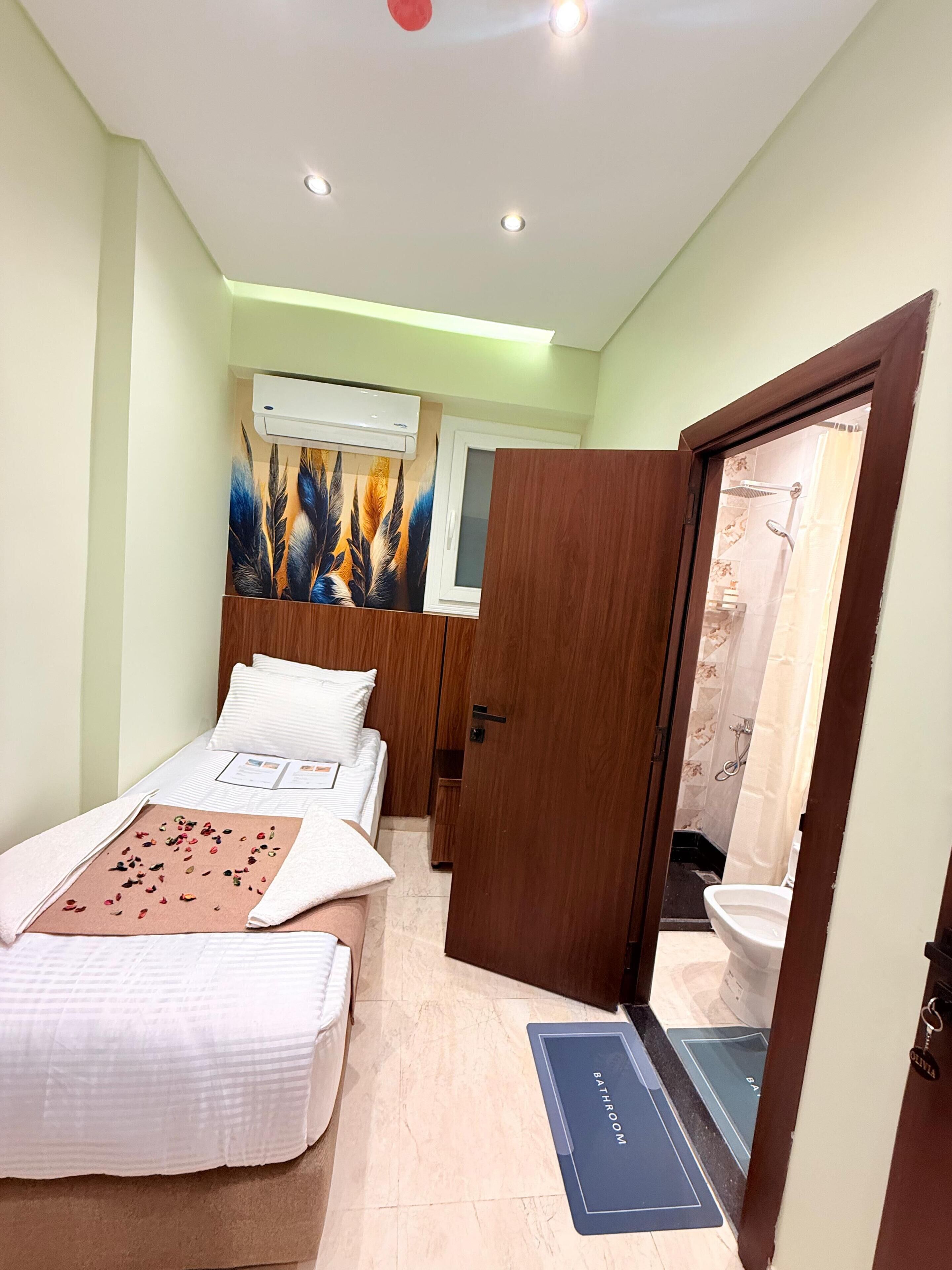 Un dormitorio con cama, armario de madera, unidad de aire acondicionado y baño visible a través de una puerta abierta.