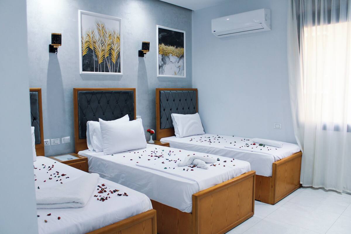 Ein Hotelzimmer mit zwei Einzelbetten, einem Nachttisch, einer Wand-Klimaanlage und zwei gerahmten Kunstwerken.