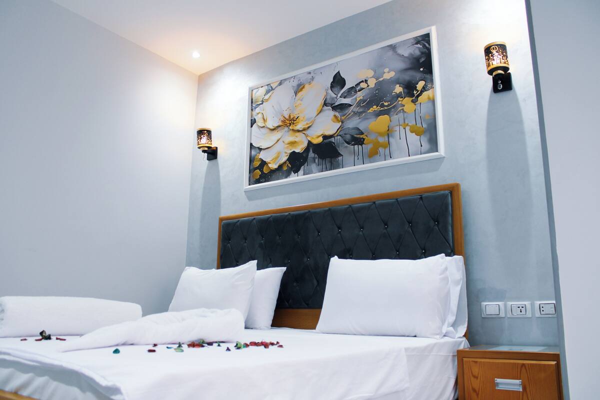 Ein Schlafzimmer mit einem großen Bett, einem Kopfteil, einem Wandbild und zwei Wandleuchten.