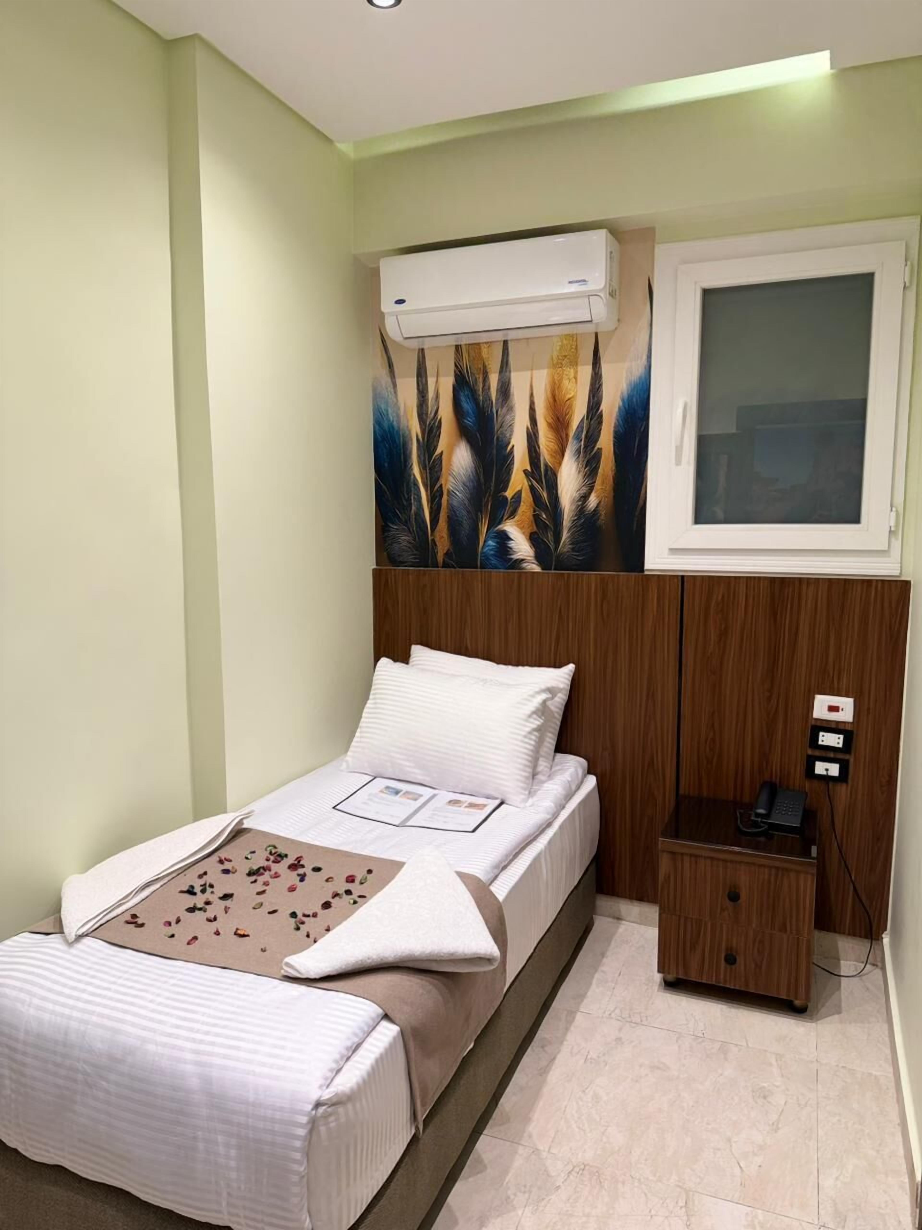 A bedroom with a bed, a nightstand, an air conditioning unit, and a window.