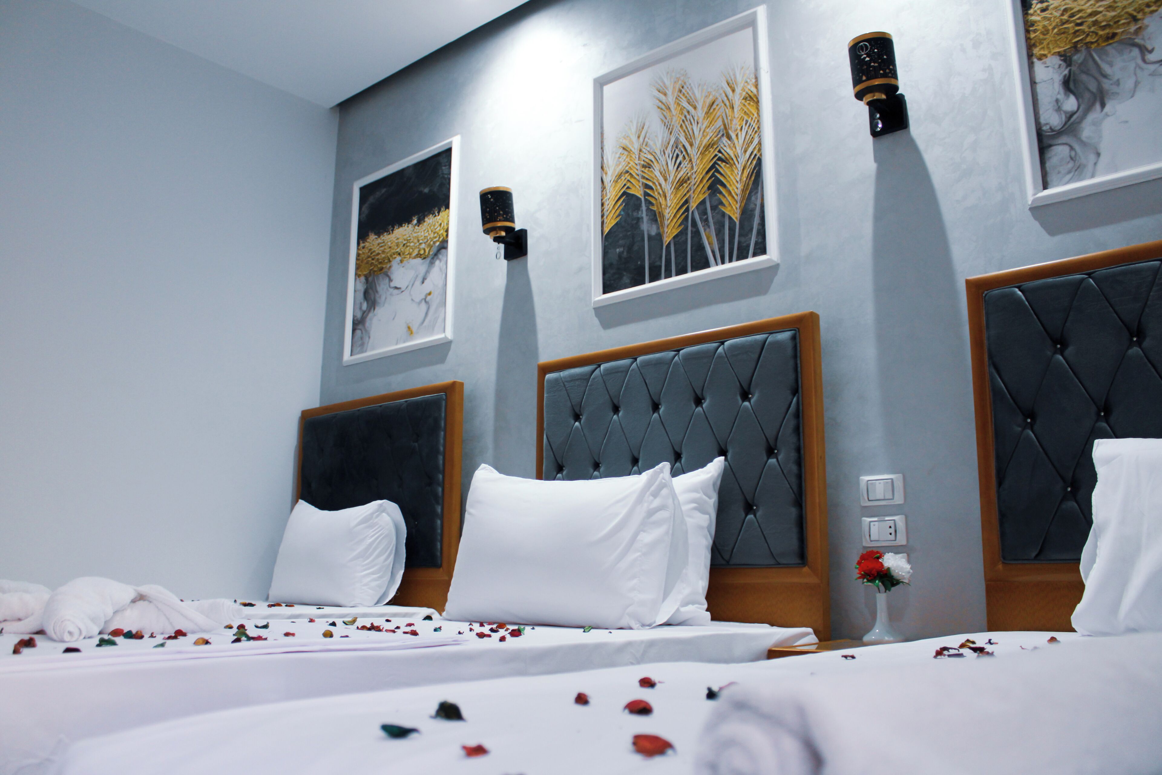A hotel room with two beds, each with a tufted headboard, white bedding, and a vase of flowers on one bed.
