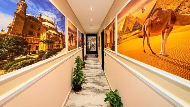 A hallway with a marble floor, potted plants, and walls adorned with large, framed pictures of historical and desert scenes. - Olivia Hotel (Cairo)