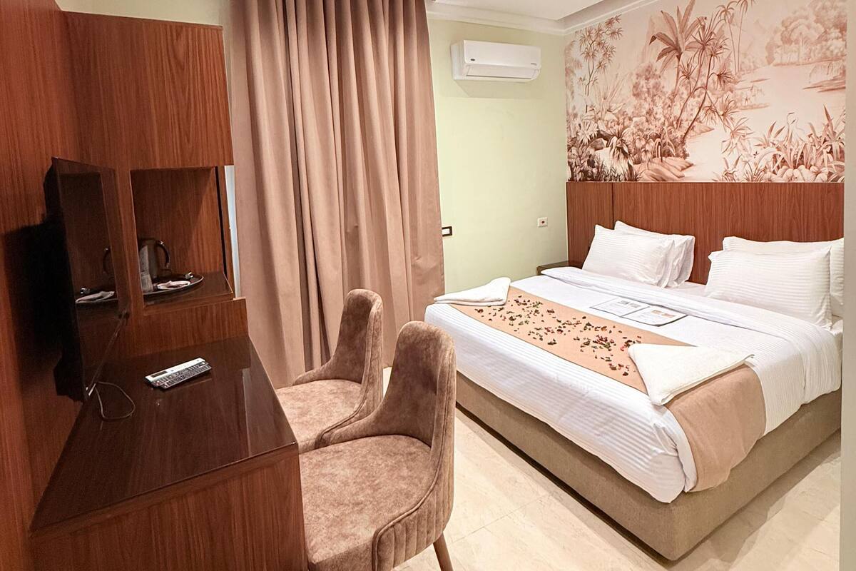 Ein Hotelzimmer mit Bett, Schreibtisch, Stuhl, Klimaanlage und Wand mit floralem Wandbild.