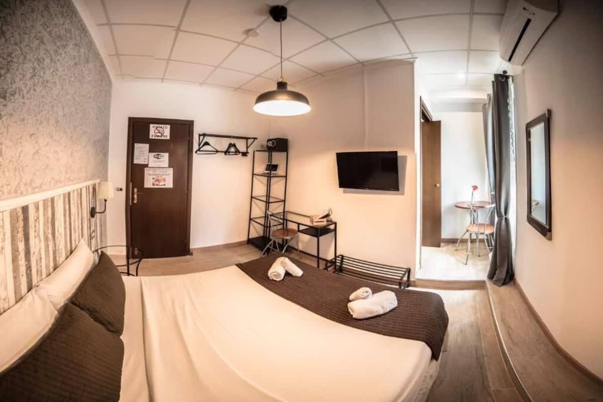 A hotel room with a bed, a desk, a chair, a TV, and a wardrobe.