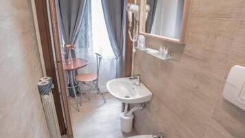 Ein Badezimmer mit zwei Waschbecken, einer Toilette und einem Spiegel. Im angrenzenden Raum befindet sich ein kleiner Tisch mit Stühlen.