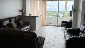 A living room with a black leather sofa, a small table, and a view through a sliding glass door to the outside. - Tortuga festival special 1Bedroom  Suite,CityView Ft Lauderdale&Two QueenBeds (Fort Lauderdale)