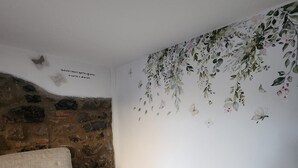 Un salon chaleureux avec un mur en pierre, un canapé beige agrémenté d’un coussin et une petite table d’appoint en bois sur laquelle sont posés un verre et une bougie.