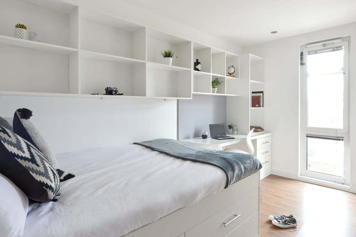 A modern bedroom with a bed, a desk, and shelves.