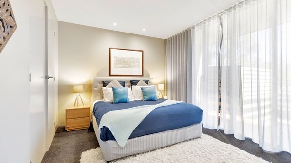 A bedroom with a bed, bedside tables, a framed picture on the wall, and sheer curtains.