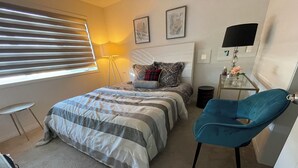 A bedroom with a bed, a blue chair, a bedside table, and a lamp.