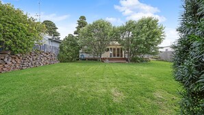 Ein Garten mit Rasen, einem Holzzaun und einem Haus mit Veranda.