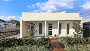 Ein modernes, zweistöckiges Haus mit überdachter Veranda, einem Weg zum Eingang und einem umzäunten Garten.