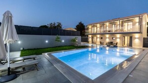A modern pool area with a rectangular pool, lounge chairs, and a covered seating area.