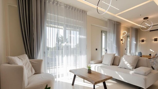A modern living room with a sofa, a coffee table, and sheer curtains.