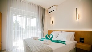 A hotel room with a bed, a nightstand, an air conditioning unit, and a window with sheer curtains.
