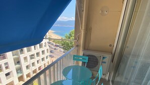 A balcony with a blue awning, a glass table, and turquoise chairs.