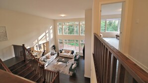 A spacious living area with a staircase, large windows, and a view of the outdoors.
