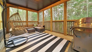 A covered outdoor seating area with a hanging chair, a sofa, and a grill.
