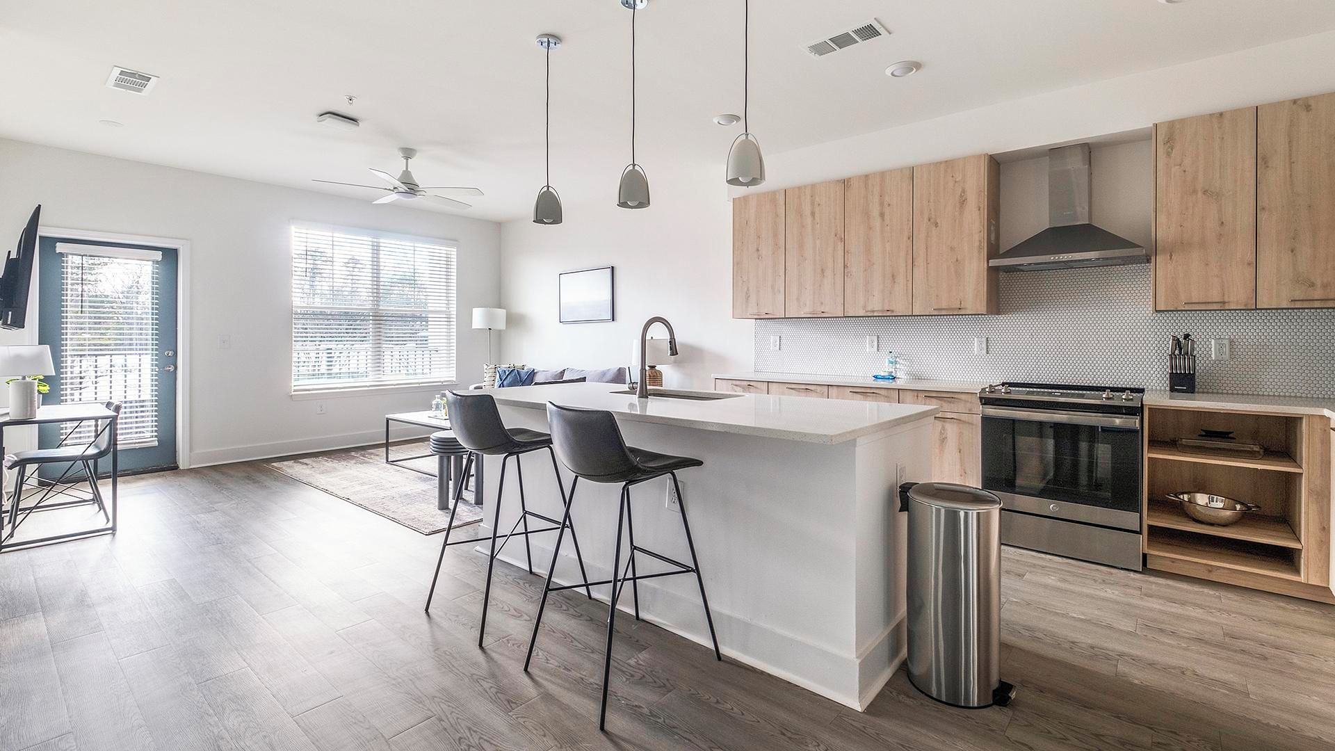 A modern kitchen with wooden cabinets, a stainless steel sink, and a large island with bar stools.