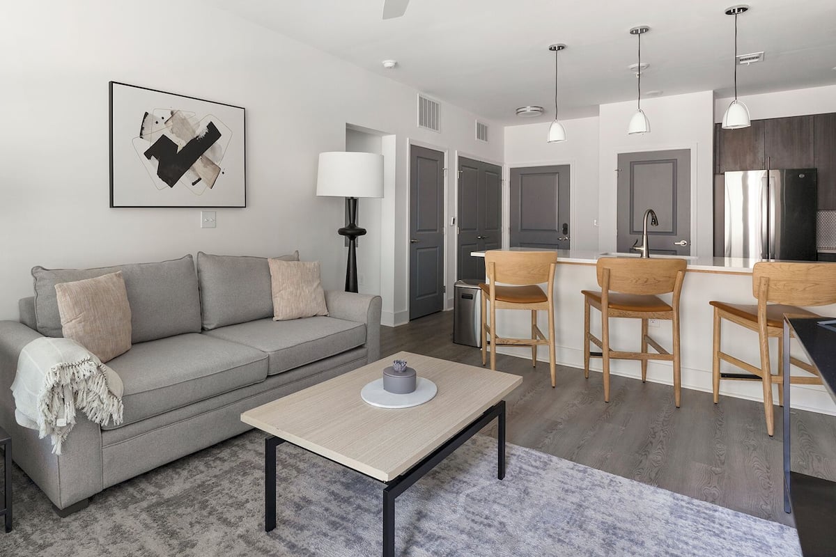 Un salon moderne avec un canapé gris, une table basse et un coin repas doté de chaises en bois.