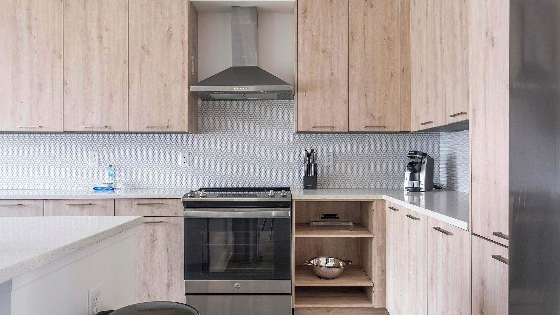 Una cocina moderna con armarios de madera clara, horno de acero inoxidable, estufa a gas y cafetera en la encimera.