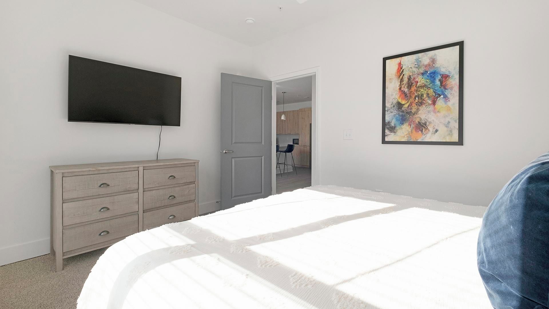 Un dormitorio con cama, cómoda, televisor y un cuadro.
