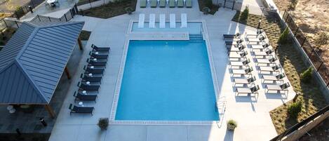 An aerial view of a hotel pool area with a rectangular pool, sun loungers, and a covered seating area.