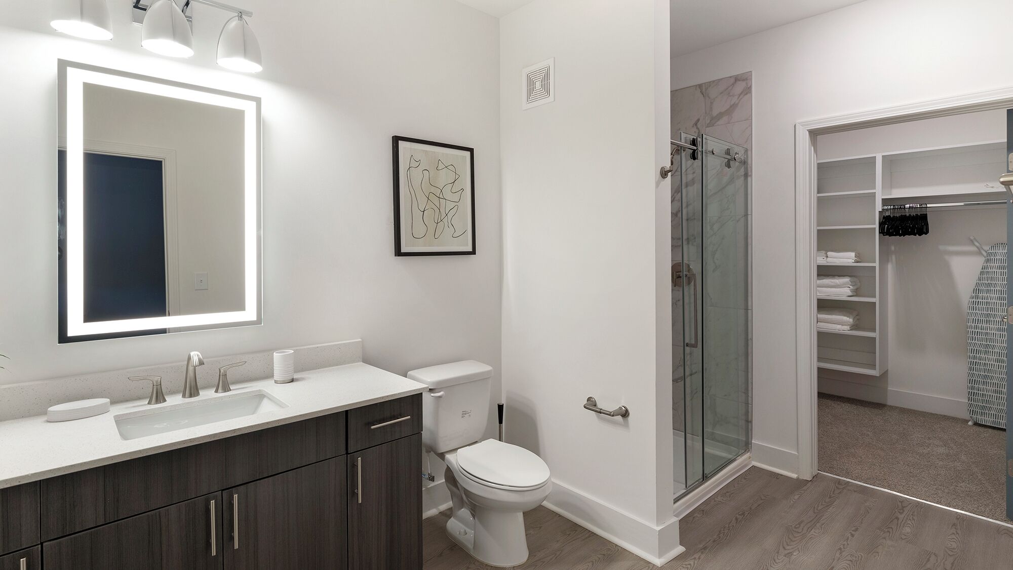 Une salle de bain moderne avec un grand miroir, des toilettes, une douche et un dressing.