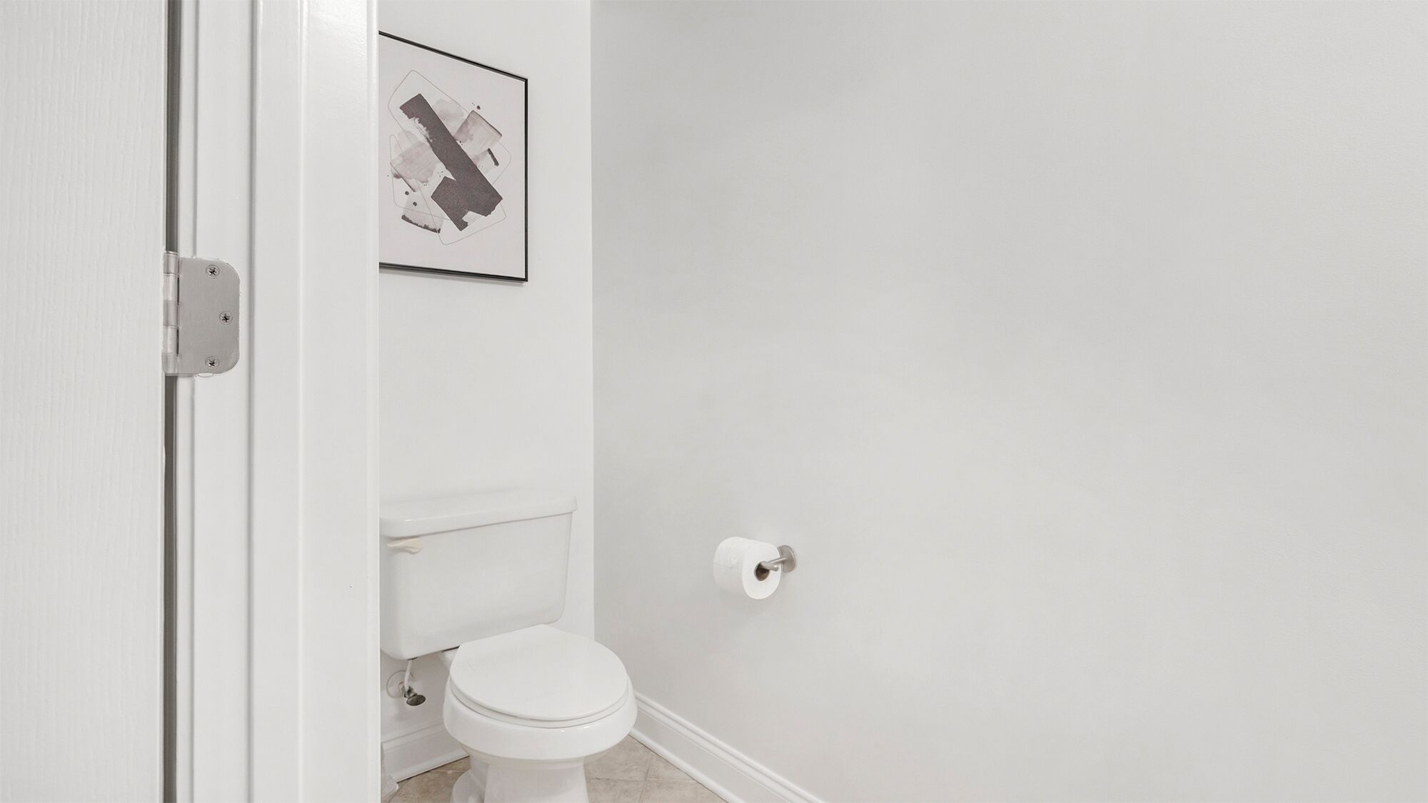A bathroom with a toilet, a roll of toilet paper, and a framed picture on the wall.
