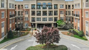 A multi-story apartment building with a central entrance, surrounded by landscaped gardens and a clear sky. - Cary Apartments by Landing (Cary)