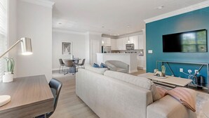 A modern living room with a sofa, a dining table, and a kitchen area in the background. - Cary Apartments by Landing (Cary)