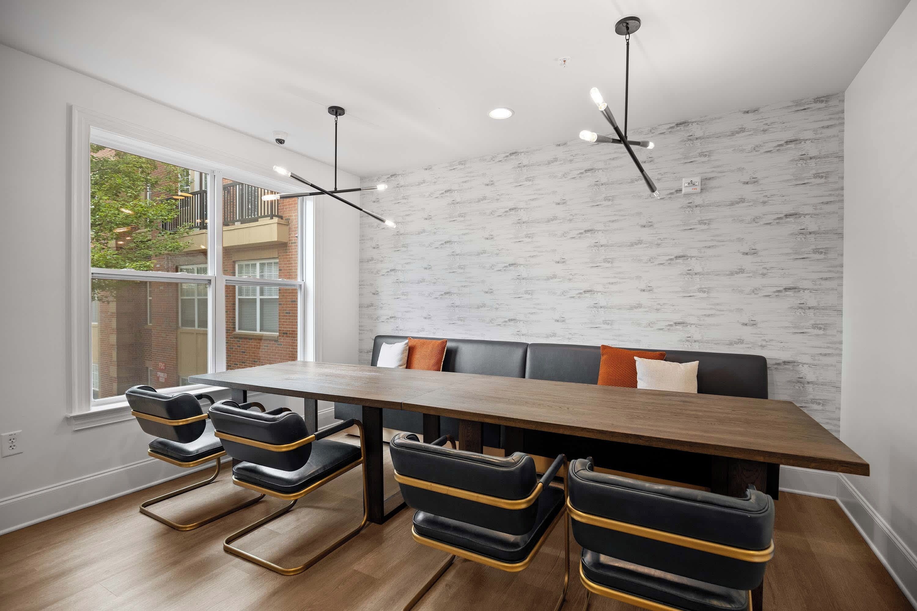 Un espace repas comprenant une table en bois, des chaises noires et dorées, un banc avec des coussins et un mur en briques blanches.