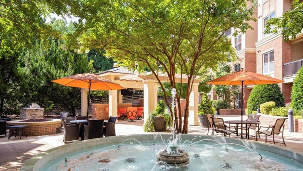 An outdoor patio area with a fountain, seating, and umbrellas. - Cary Apartments by Landing (Cary)