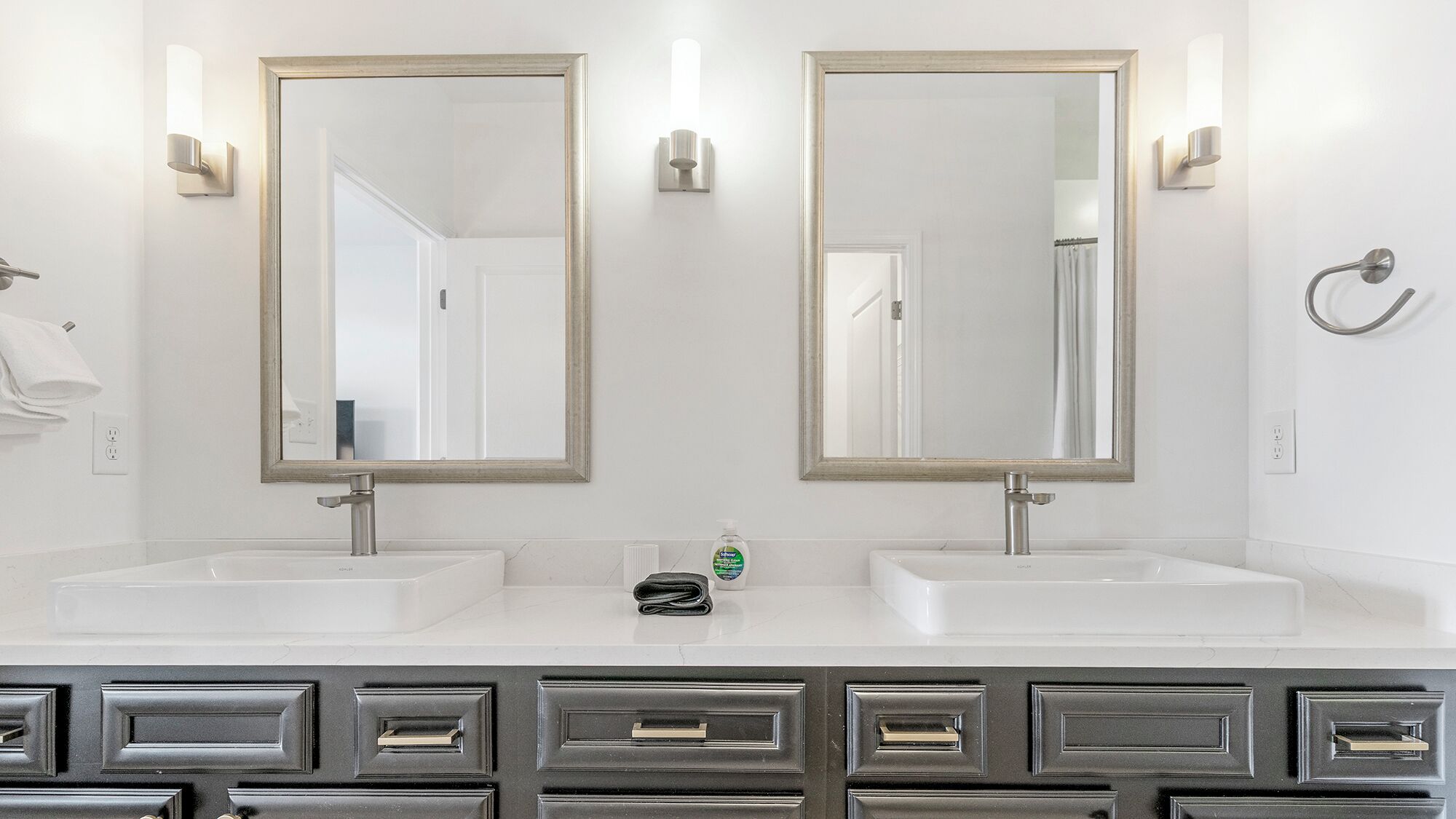 A bathroom with two sinks, two mirrors, and a towel rack.