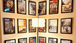 Un salon avec un canapé bleu foncé, une lampe et un mur décoré de couvertures du magazine « POST » encadrées.